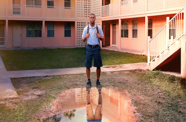 David, dressed in his school uniform, stands in front of a big puddle in the middle of his housing project
