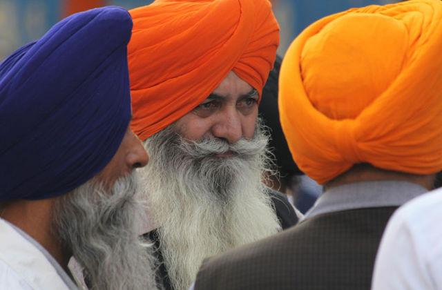 People in blue, orange and yellow turbans with long beards look into the distance.