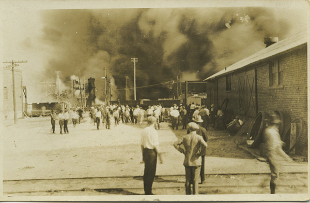1921 Tulsa Massacre. Archival photo of people standing and looking at smoke rising.