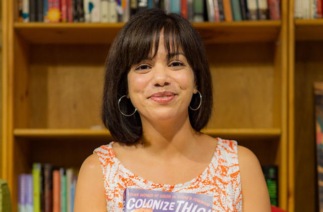 Daisy Hernández. Latinx person with dark bob haircut, brightly colored top and book in hands.