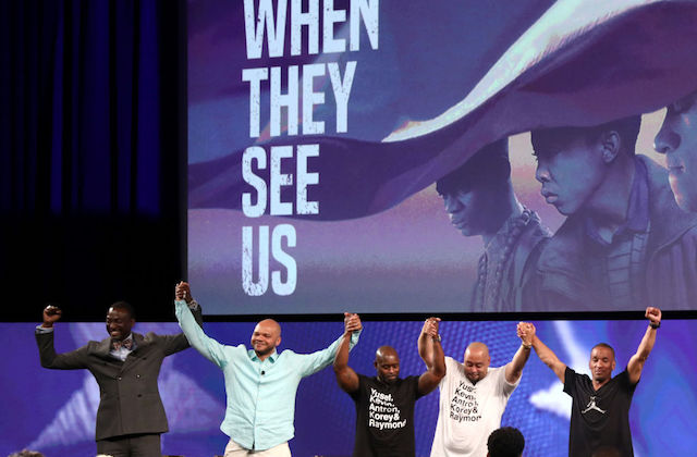 Yusef Salaam, Kevin Richardson, Anton McCray, Raymond Santana and Korey Wise. Five men of color hold hands on stage with movie image projected behind them on screen.