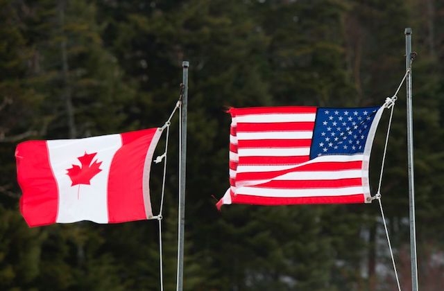 Red and white Canadian flag and red, white and blue American flag fly next to each other at the U.S.-Canada border.