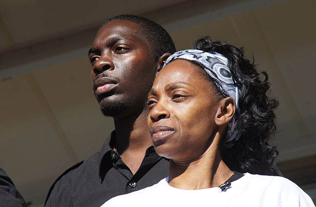 ALWAYS IN SEASON. Photo from a documentary showing an older Black woman with curly dark shoulder-length hair wearing a blue and white headband and white T-shirt, standing next to young Black black with short dark hair and short facial hair wearing a black button up shirt.