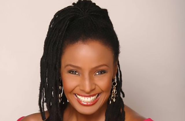 B. Smith. Black woman with long dark locs pulled into high ponytail, wearing off-the-shoulder top.