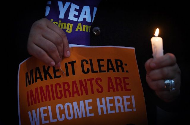 close up of a person holding a lit candle next to a sign that reads, "make it clear, immigrants are welcome here"