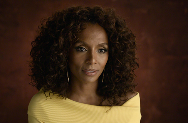 Janet Mock. Black woman with brown shoulder-length curly hair wearing a yellow top.