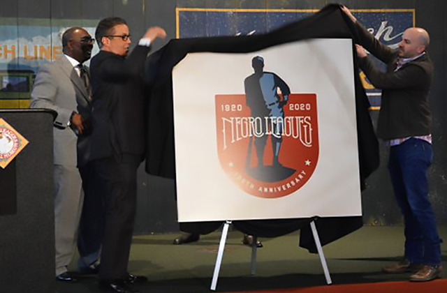Negro League Logo. A white board featuring the logo illustration of a Black baseball player being unveiled by two men.