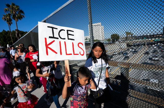 A young boy stands at a protest and holds a sign that reads "ICE KILLS" 