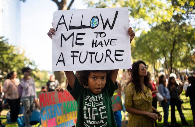 Black child in black shirt at protest holds white sign that reads, "Allow me to have a future."