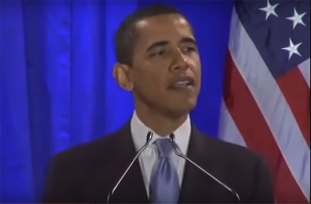 Barack Obama. Black man with short dark hair wearing a dark suit jacket, blue tie and white shirt standing in front of a blue curtain and the American flag.