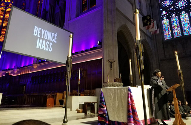 Beyonce Mass. Church setting with a Black woman at an altar and a digital sign on stage reading "Beyonce Mass."