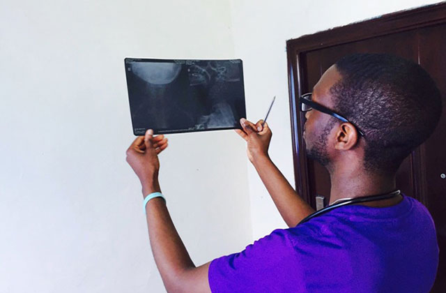 Medical Professional. Black person wearing blue hospital scrubs turned away looking at screen.