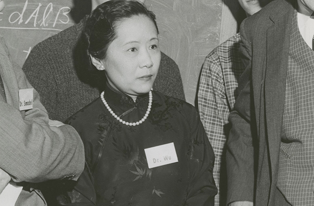 Chien-Shiung Wu. Black and white photo of Asian woman with dark hair pulled back wearing dark high-collar top with pearls and name tag.