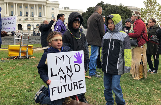 Native American Land Protest. Three young boys stand around a sign reading "My land my future."