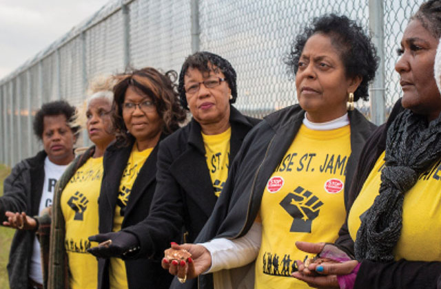RISE activists. Six older Black women standing side-by-side against a fence holding a hand out, all wearing yellow t-shirts and black jackets.