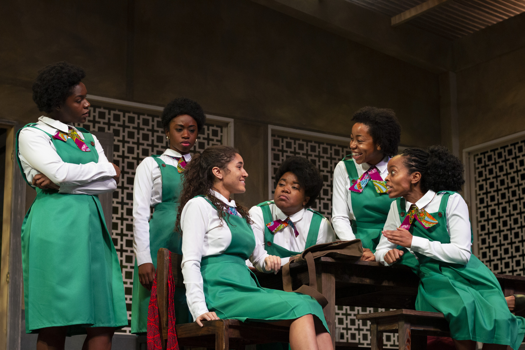 School Girls. Six Black teenagers wearing uniforms of green dresses and white shirts on stage.