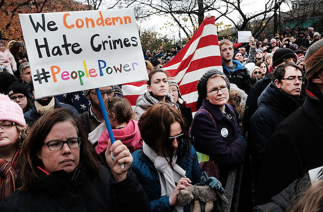 Woman surrounded by others at a rally holds a sign that reads, "We Condemn Hate Crimes"