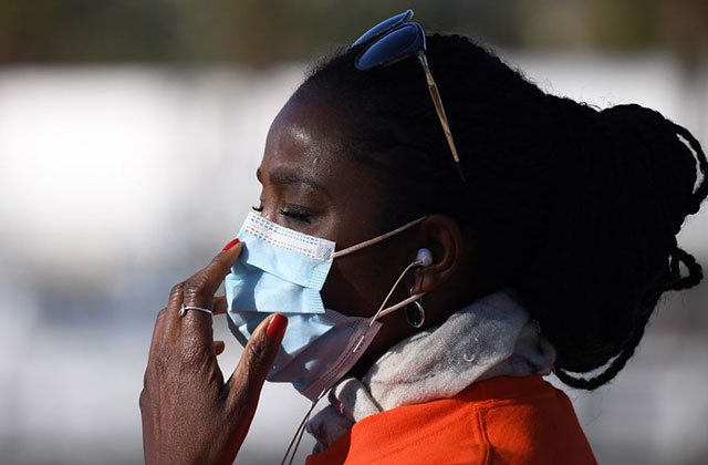Mask. Black woman with dark hair wearing a white face mask, white scarf and orange coat.