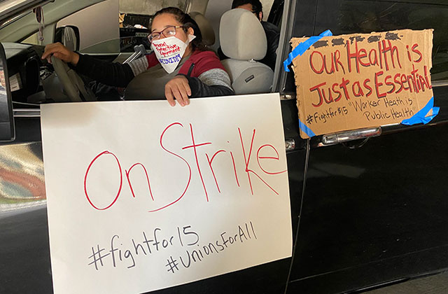 Fast food protest. Latinx woman in car wearing a face mask in black car holding a white sign that reads: On Strike #fightfor15 #unionforall