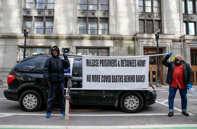 two men hold a protest sign calling for the release of prisoners and detainees from U.S. jails and prisons.