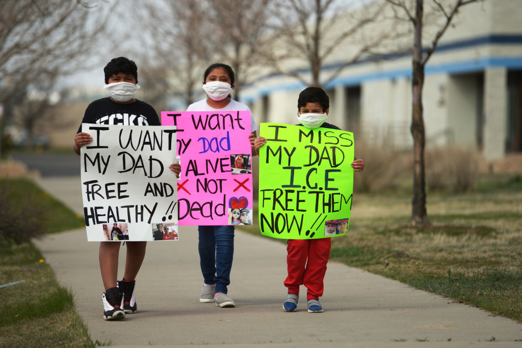 three Latinx children a boy, 10, a girl, 11, a boy six, hold signs in front of them like "I don't want my dad free and healthy"