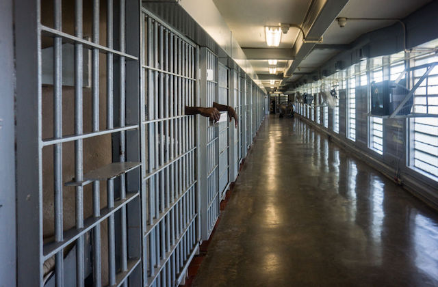 A row of prison cells with a person's arms shown hanging through some of the bars.