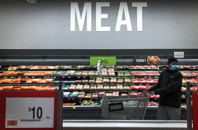 Meat. Black man wearing blue face mask, dark jacket and blue jeans, in a supermarket in front a sign that reads, "Meat."
