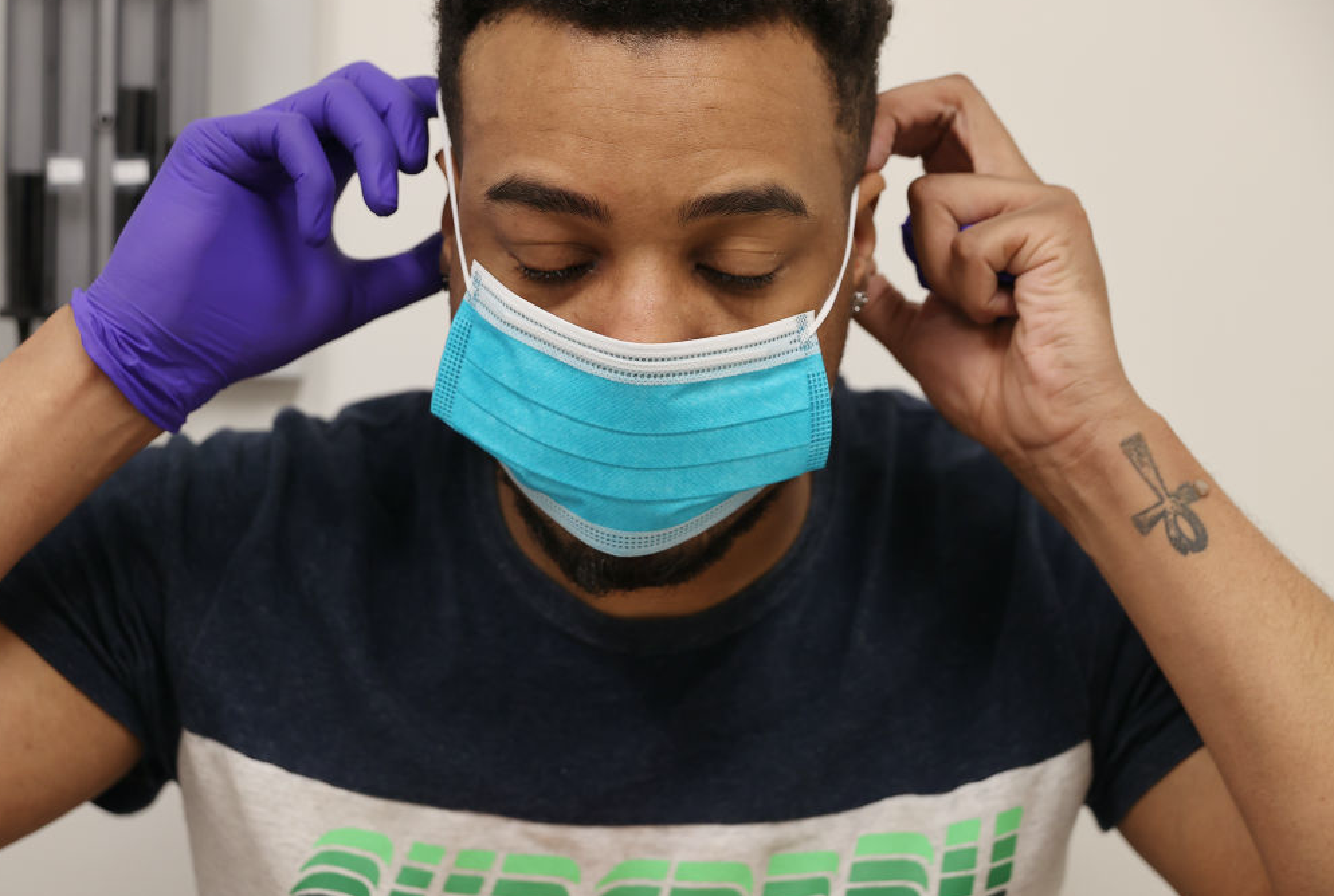 Black Man Takes Coronavirus Test. Young black man with blue mask on and one purple medical glove on in medical setting.