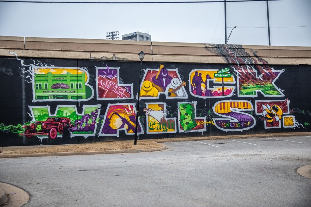 Black Wall on side of highway with the words "Black Wall St." in thick block graffiti color letters against a black wall