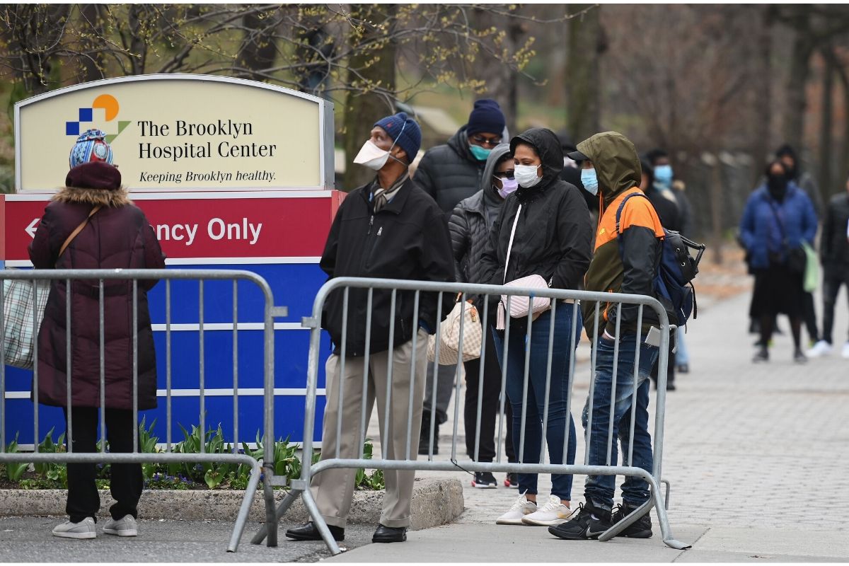 Mostly African Americans stand in line behind a metal barricade with masks on outside of The Brooklyn Medical Center