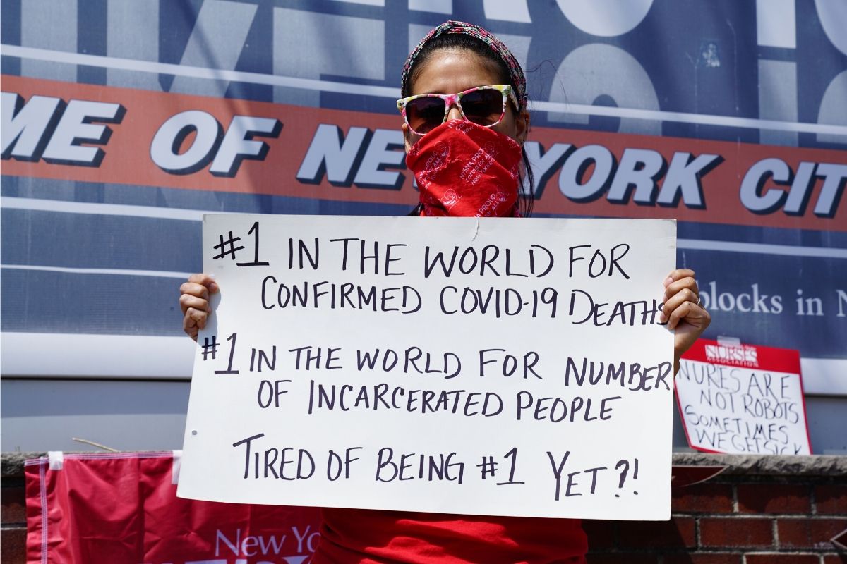 Black woman with mask stands in front of Rikers Island Jail Complex sign 