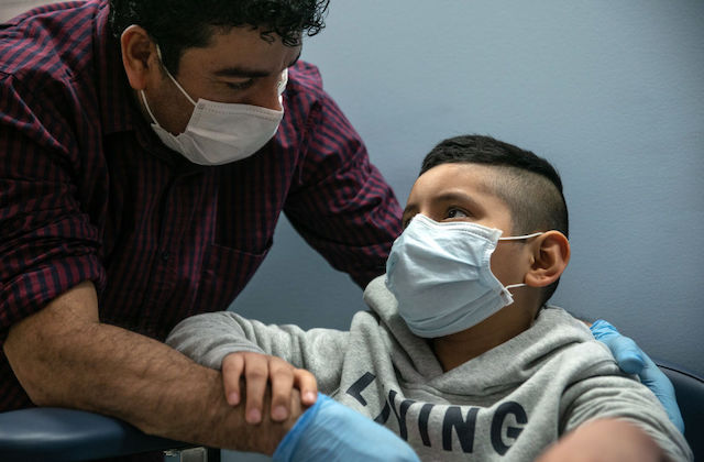 A father and son, both wearing face masks, look into each other's eyes..