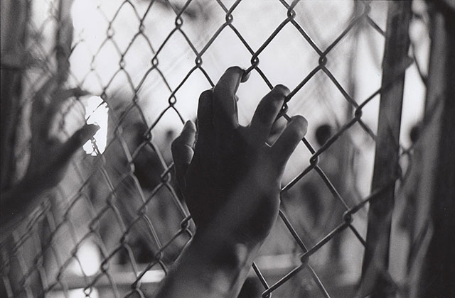Criminal justice. Black and photo of male hands holding onto a gate.