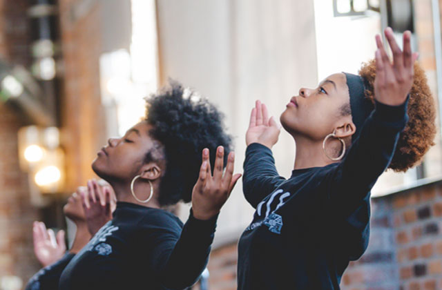 Love is Healing Fund. Two young Black women with Afros wearing black tops with both arms raised.