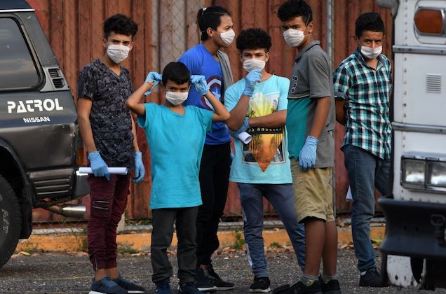 four young Honduran boys stand next to each other and wear white face masks.