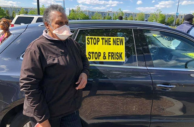 NYPD Protest. Older Black woman with short gray hair wearing white face mask and black jacket standing in front of black car with sign in window that reads: Stop the new stop & frisk.