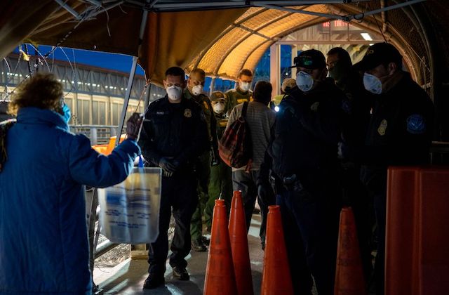 Border patrol officers at the southern border wear white face masks as they check someone's ID.