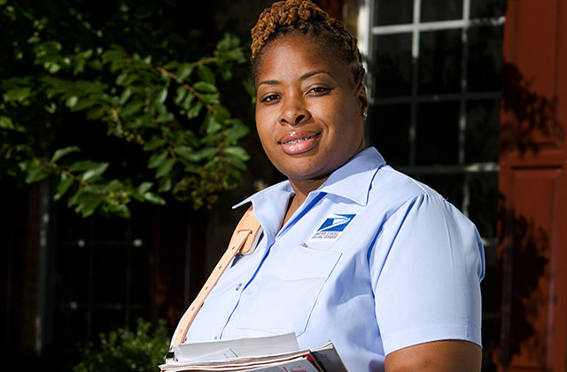 USPS. Black woman postal worker with brown braids wearing a blue shirt.
