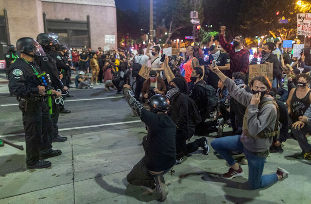 Protesters kneel before a group of armed police officers.