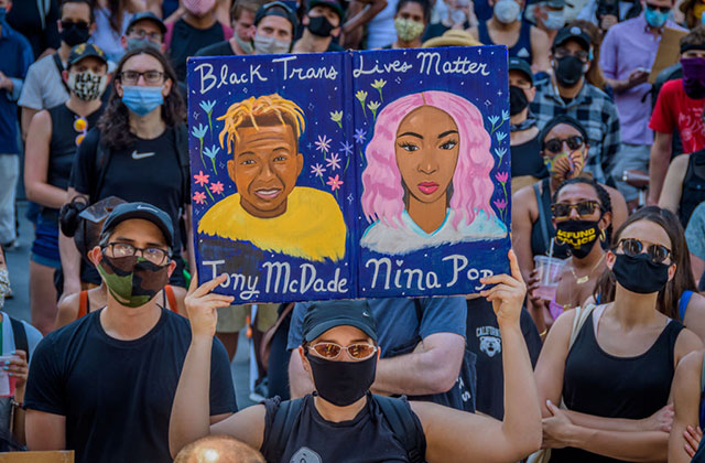 Black Trans Lives Matter rally. Man in a crowd holds up colorful drawing of Tony McDade and Nina Pop.