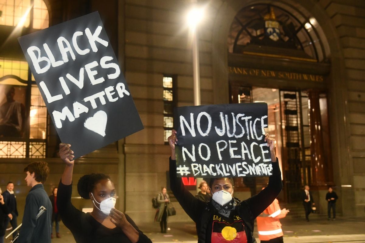Two young black women holding "Black Lives Matter" and "No Justice, No Peace" wearing black shirts and masks.