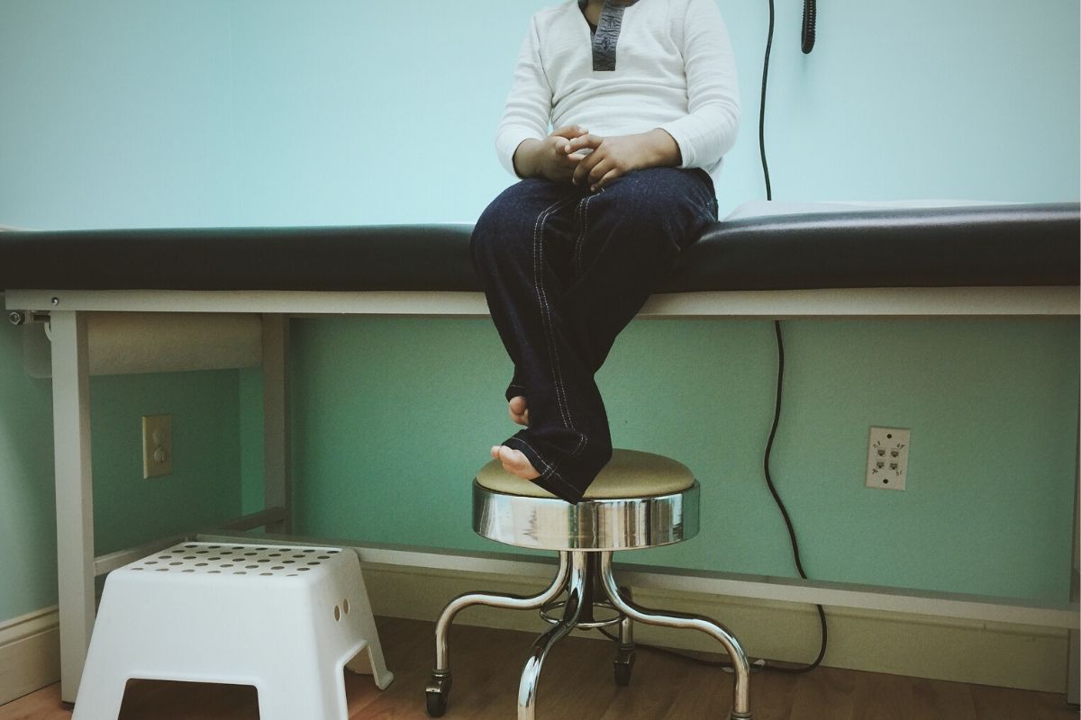 Shot of person waiting in a doctors office. Sitting on a table, with jeans on and barefoot