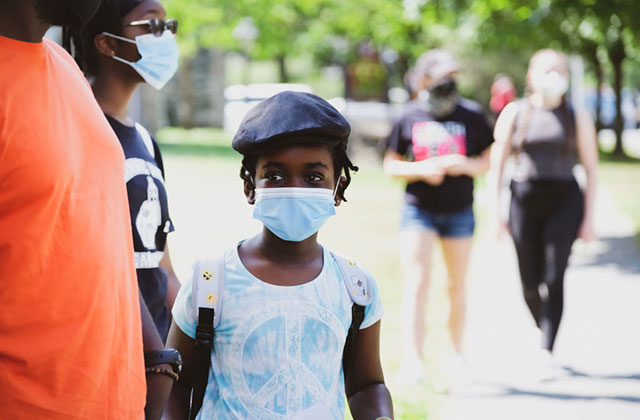 Little girl mask. Young Black girl wearing surgical mask, blue hat and white tee.