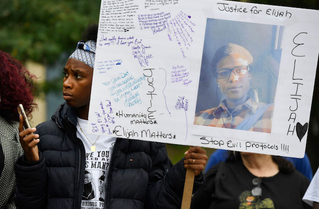 Black protester holds poster showing image of young Black man wearing black eyeglasses.