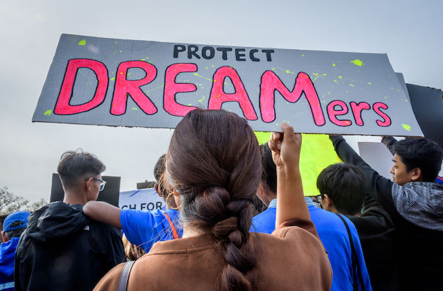 A woman with a long braid holds a sign that reads, "Protect Dreamers"