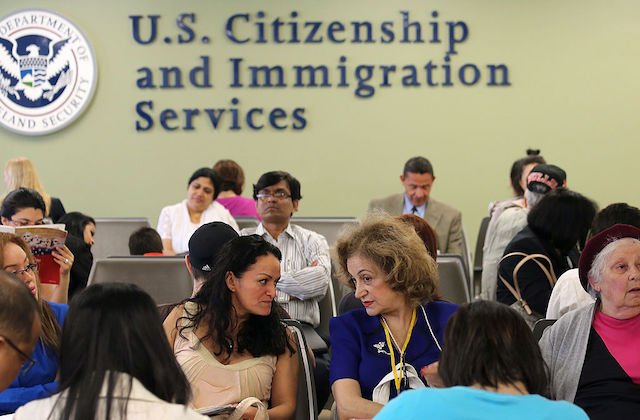 A group of people are seated below a large sign on a wall that reads, U.S. Citizenship and Immigration Services.