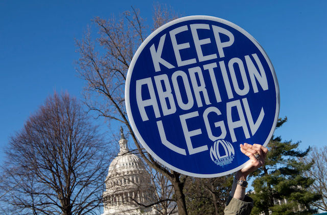 A hand holds a sign that reads "Keep Abortion Legal" in front of the US Capitol and under a clear blue sky