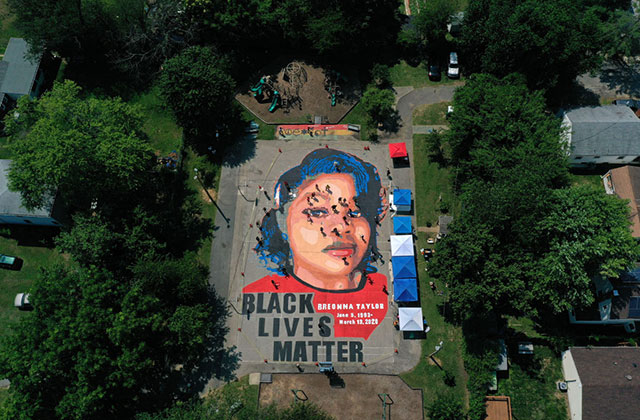 Breonna Taylor mural. Large paining on ground surrounded by trees in a neighborhood of a young Black woman with blue hair and red shirt.
