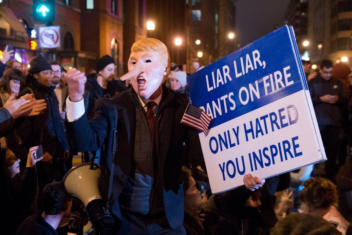 Protest with a man with a Trump mask on with a long Pinnochio like nose and a sign reading "Liar Liar, Pants on Fire Only hatred, you inspire"