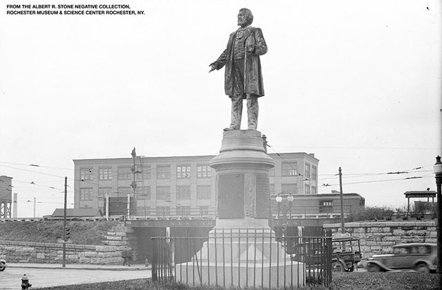 Frederick Douglass monument. Black and white photo of statue of a Black man on a tall pedestal in the city of Rochester, N.Y.